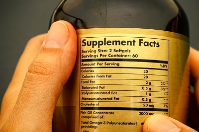 Glass jar with supplement facts in a person's hands.