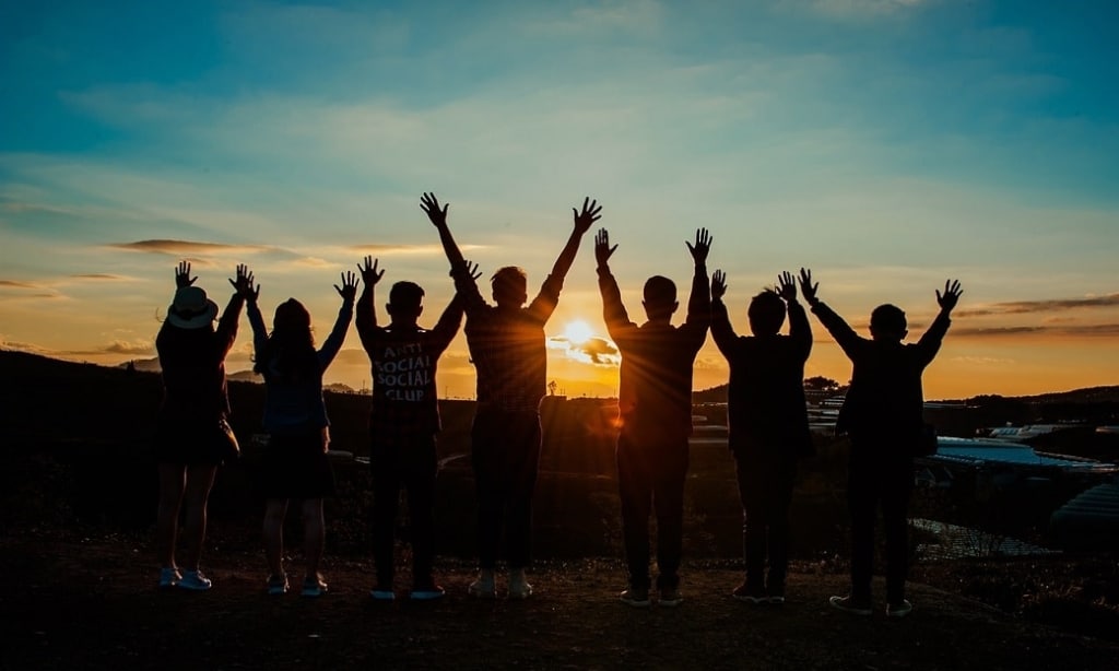 A group of people with arms raised in affirmation are silhouetted against a sunrise.