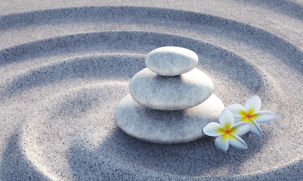 stacked stones and blossoms within a swirl of sand symbolize calm, wholeness, and integration